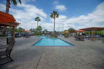 A pool surrounded by palm trees and a patio area.